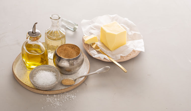 A imagem mostra manteiga e outros ingredientes que podem temperar alimentos, como sal, açúcar, azeite e vinagre.